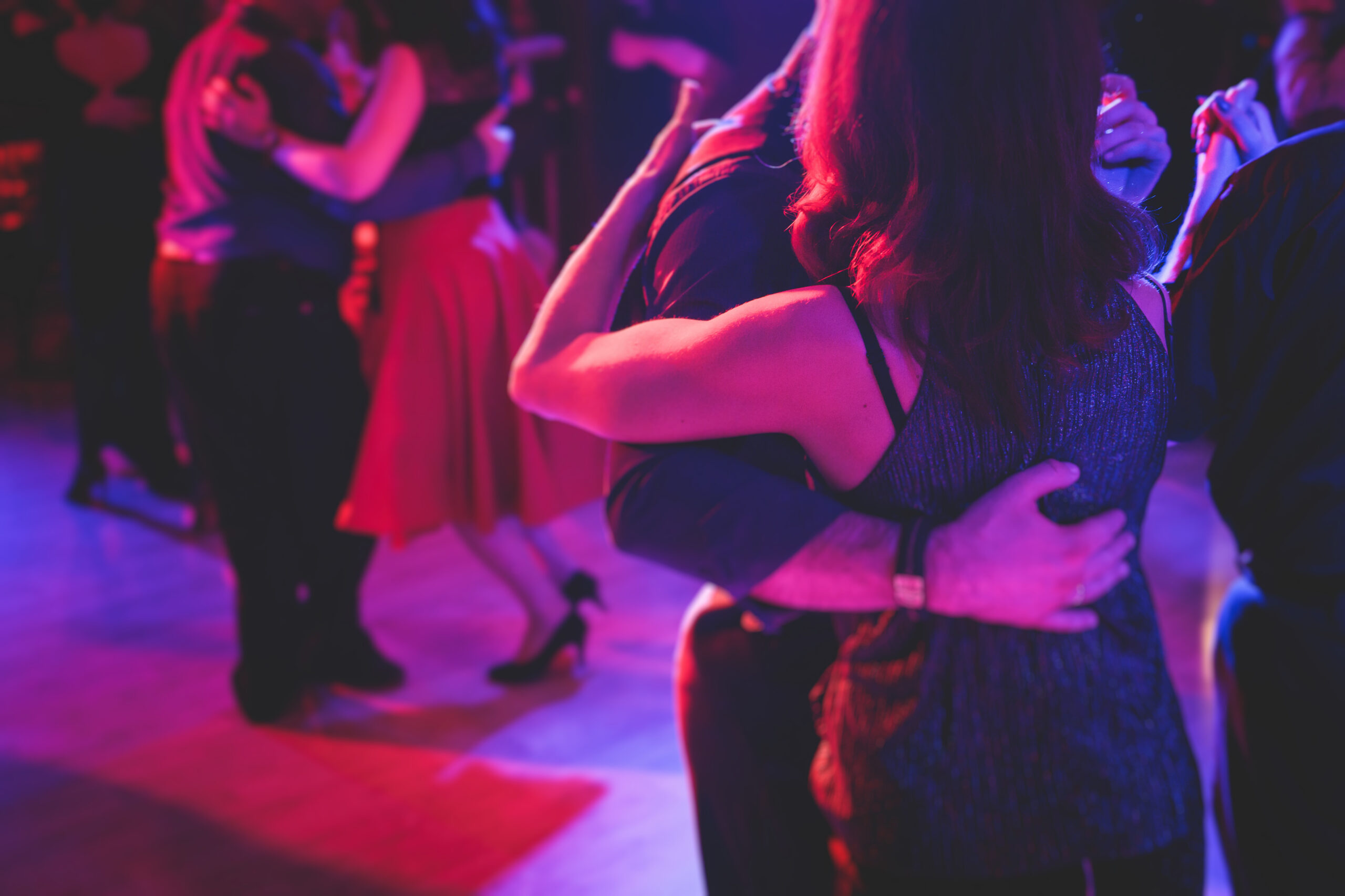 Couples dancing traditional latin argentinian dance milonga in the ballroom on a festival, tango studio, salsa, bachata and kizomba lesson in the red and purple lights, rehearsal in the dance class