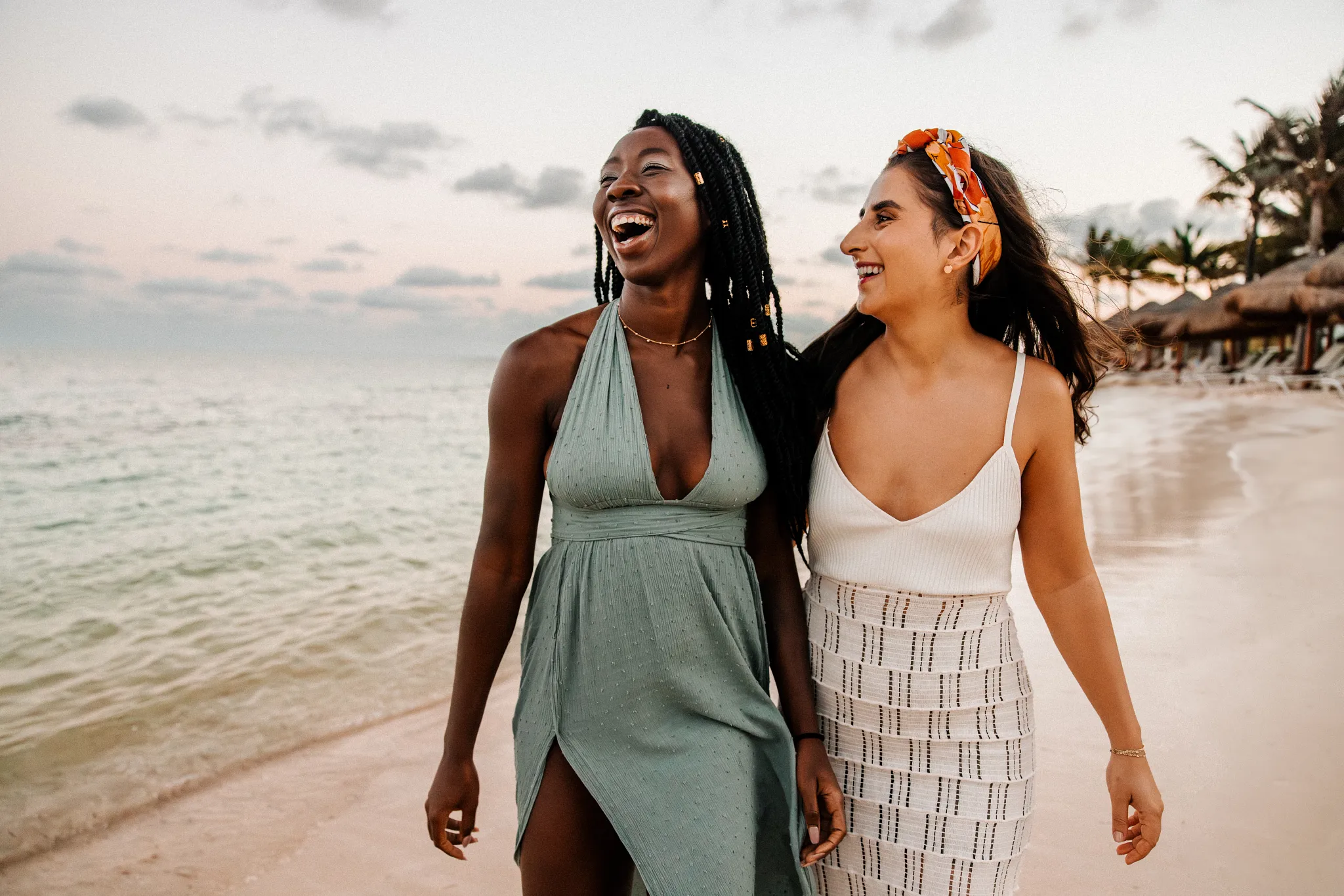 Two women laughing while walking along the beach during golden hour at Breathless Riviera Cancun.