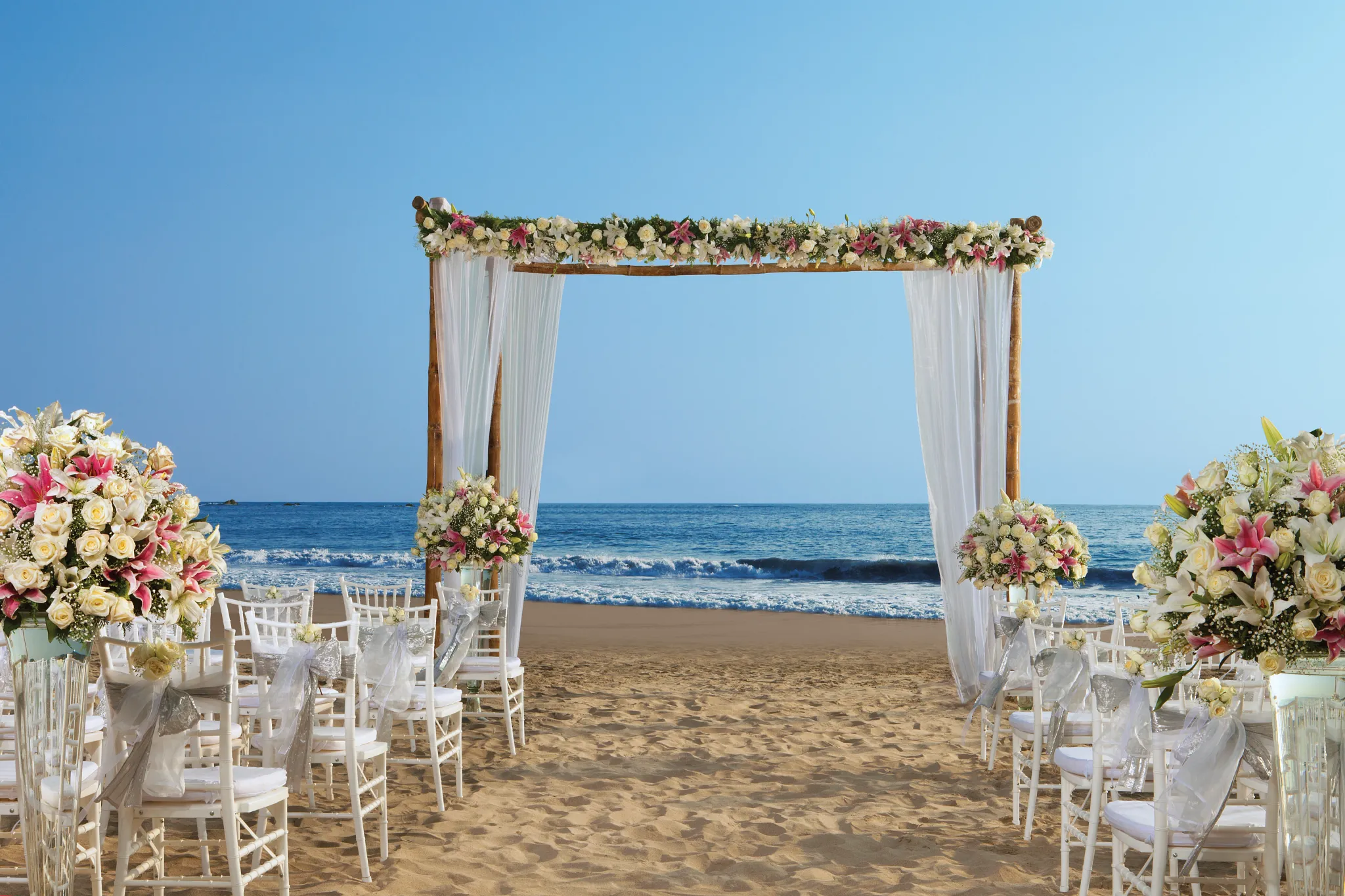 Beach wedding ceremony with floral arch and white chairs at Secrets Vallarta Bay Puerto Vallarta