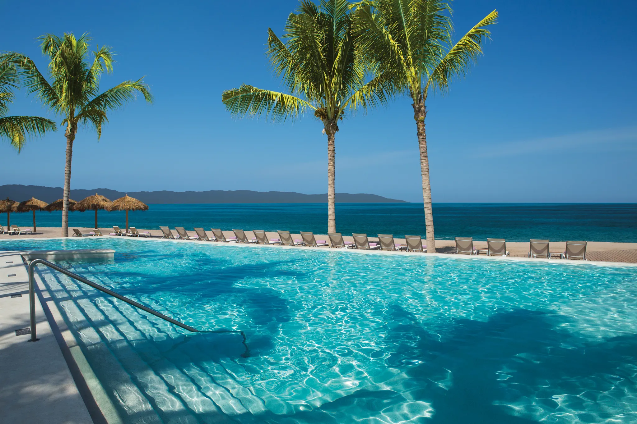 Infinity pool overlooking the beach with lounge chairs and palm trees at Secrets Vallarta Bay Puerto Vallarta.