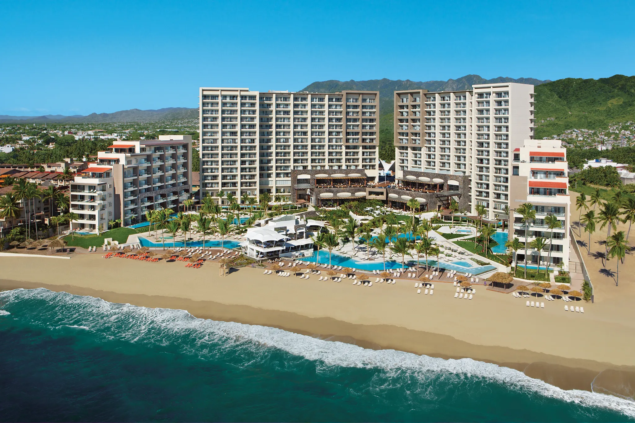 Wide aerial shot of Secrets Vallarta Bay Puerto Vallarta with modern buildings, pools, and beachfront access.