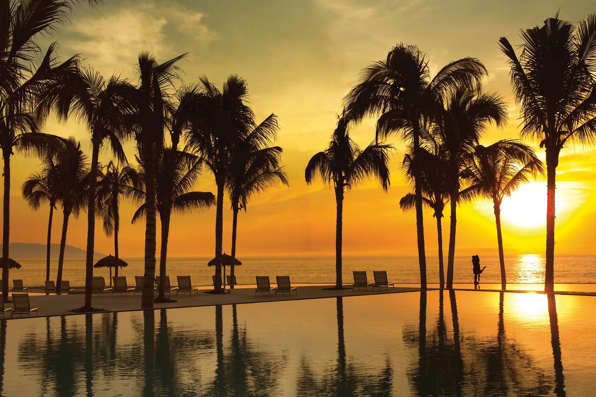 Silhouetted couple by a palm-lined infinity pool at sunset at Secrets Vallarta Bay Puerto Vallarta.